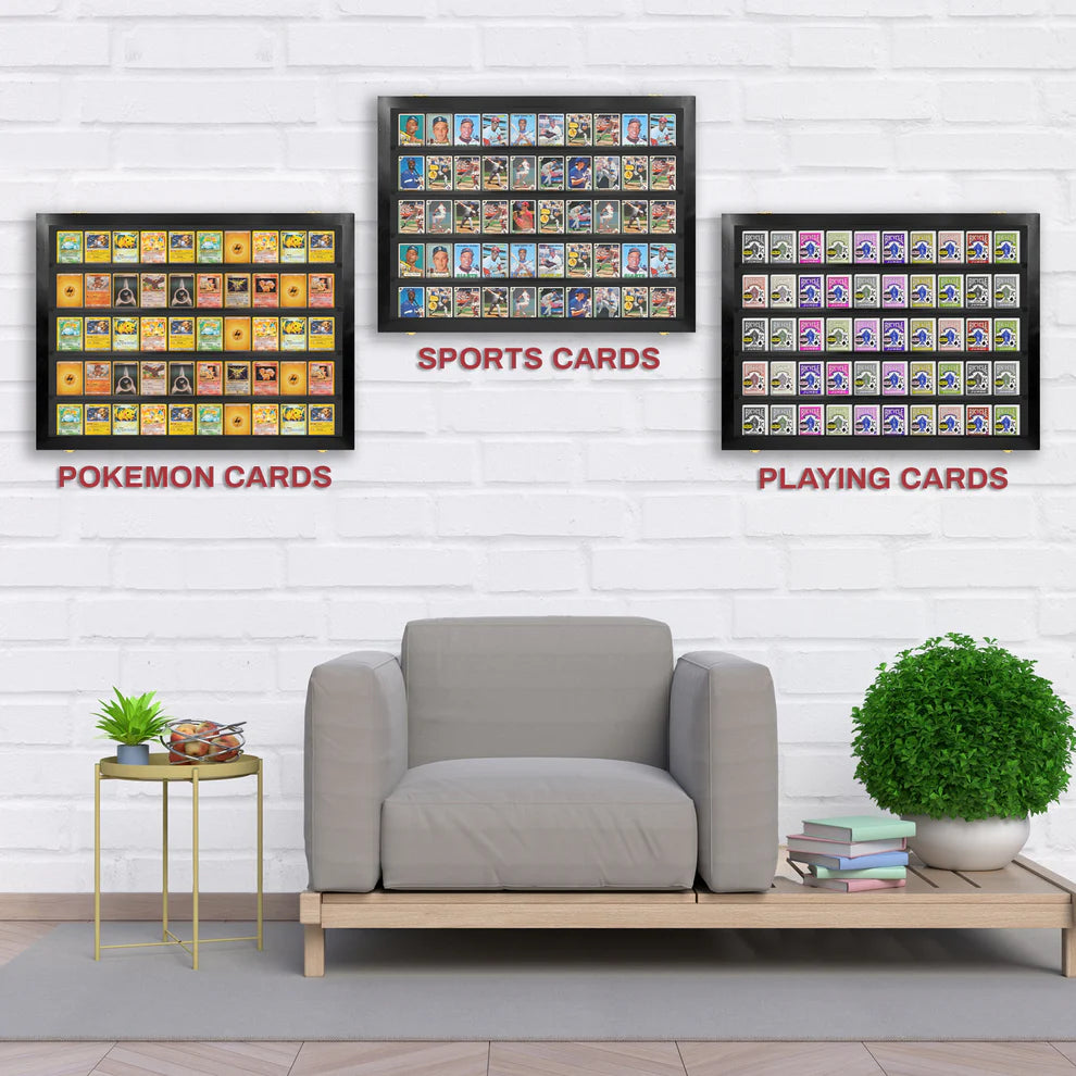 Framed collections of Pokemon cards, sports cards, and playing cards on a wall above a gray armchair.