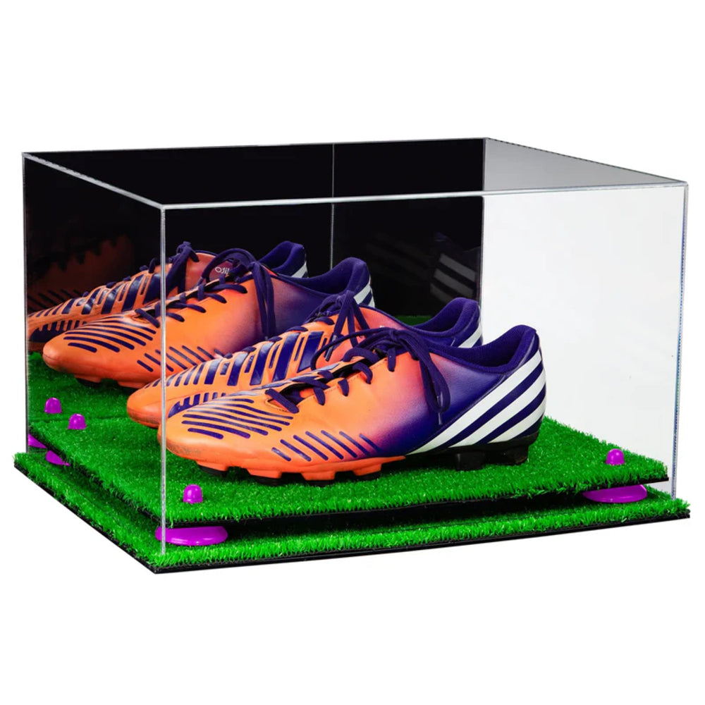 Two pairs of orange and purple soccer cleats in a clear display case on a grass-like surface.