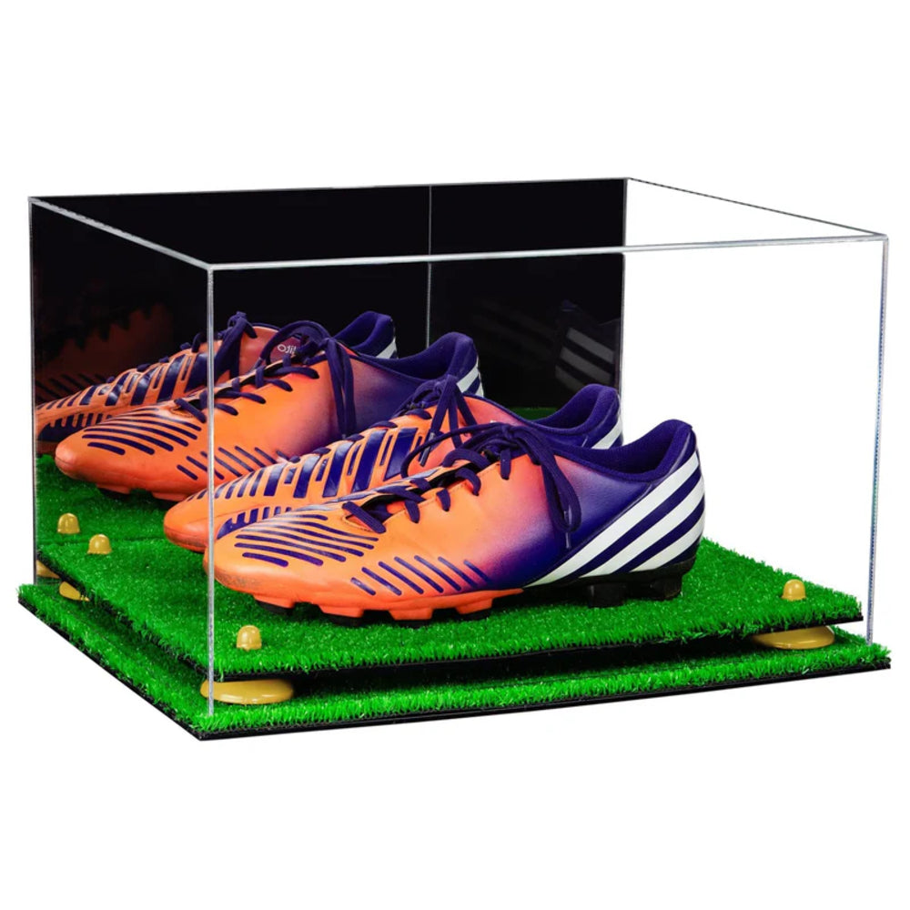 Pair of orange and purple soccer cleats in a clear display case on a grass-like surface.