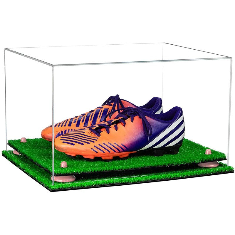 Orange and purple soccer cleats in a clear display case with grass-like surface