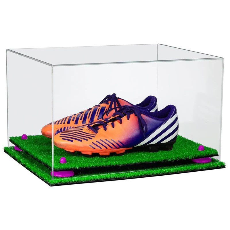 Orange and purple soccer cleats in a clear display case with grass-like surface