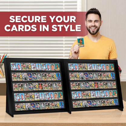 Man holding a trading card with two large display cases filled with cards on a wooden surface.