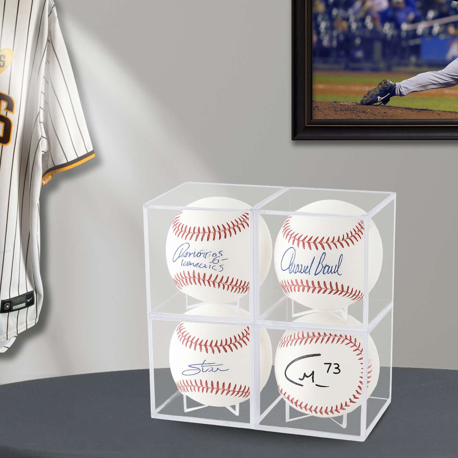Four autographed baseballs in a clear cube display with sports-themed decor in the background.