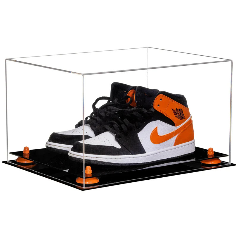 Black, orange, and white sneakers in a clear display case on a white background