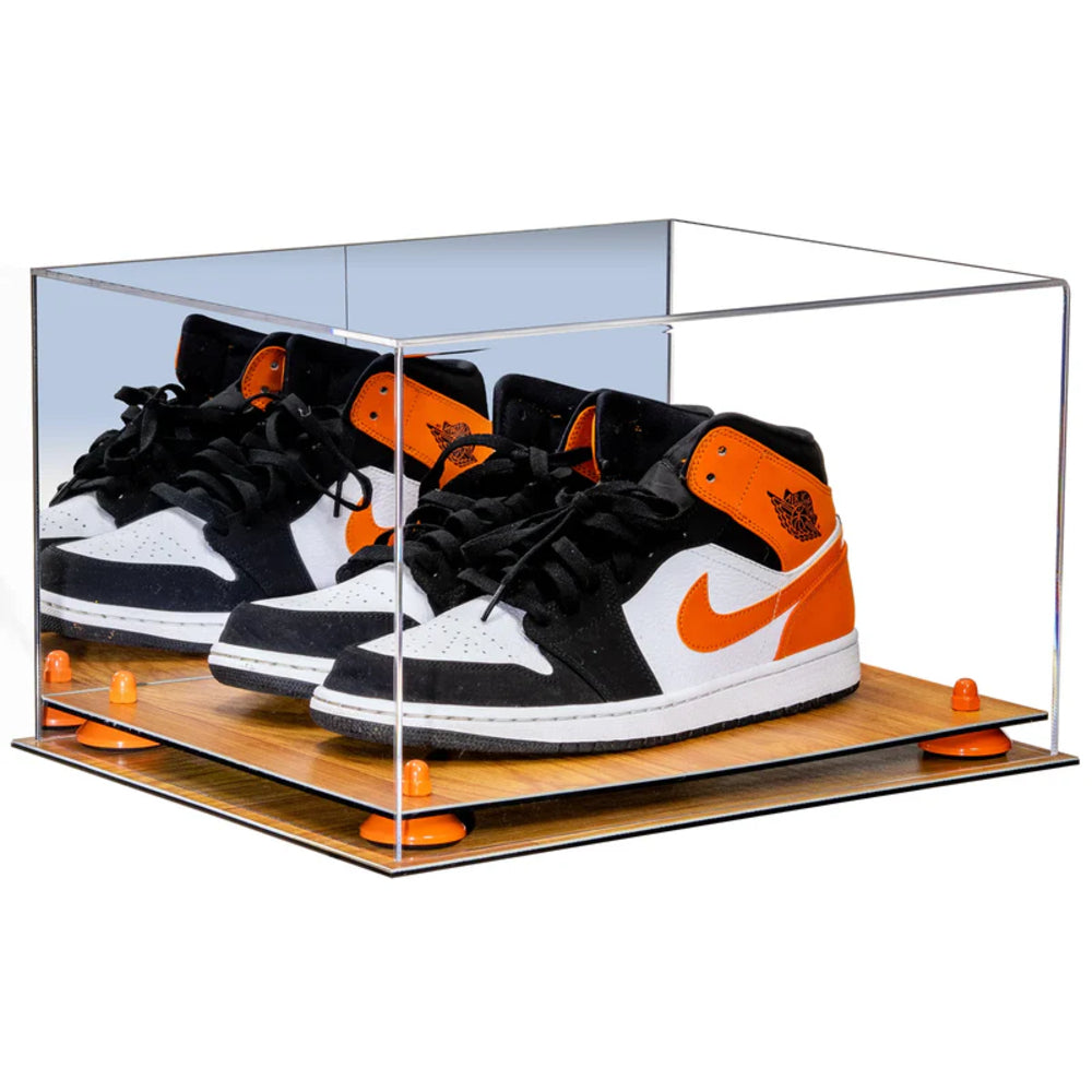 Black, orange, and white sneakers in a clear display case on a wooden base.
