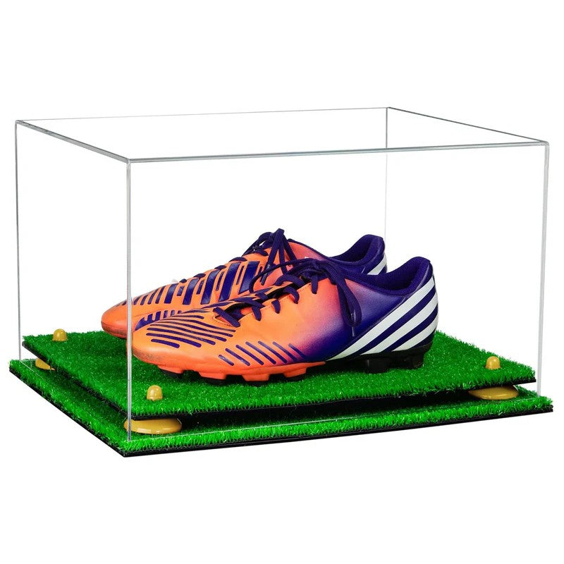 Orange and purple soccer cleats on a grass-like surface inside a clear acrylic display case.